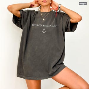 May include: Pepper-colored oversized t-shirt with the text "DIBS ON THE SAILOR" in white, above a small anchor graphic. The shirt has short sleeves and a relaxed fit, perfect for casual wear.