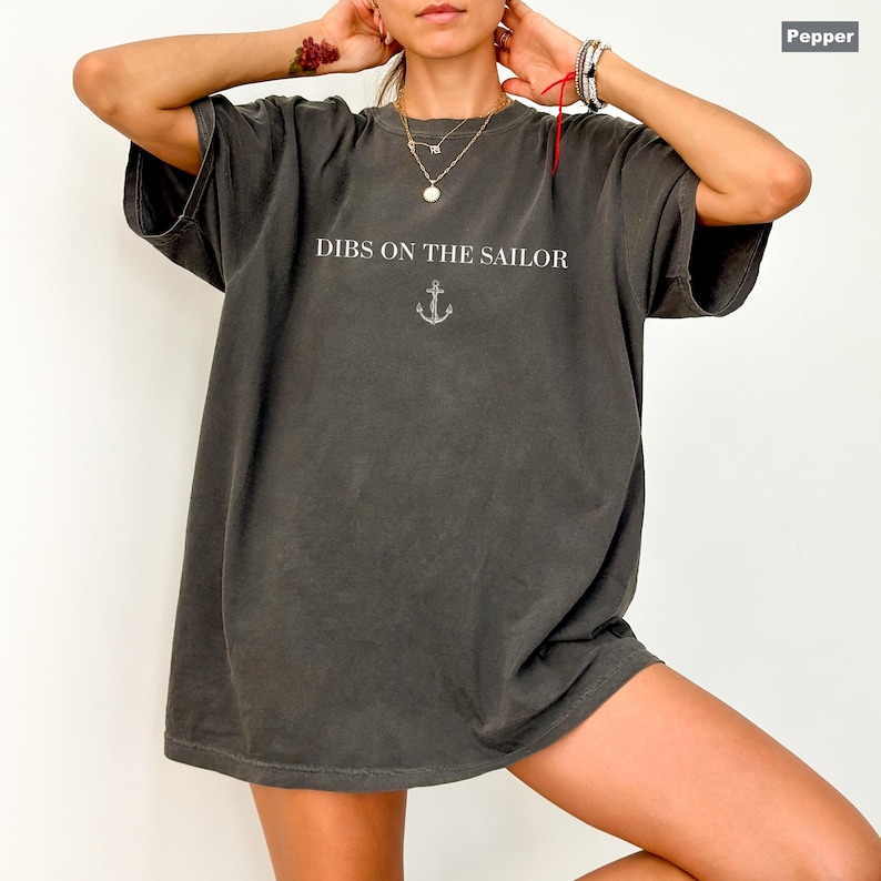 May include: Pepper-colored oversized t-shirt with the text "DIBS ON THE SAILOR" in white, above a small anchor graphic. The shirt has short sleeves and a relaxed fit, perfect for casual wear.