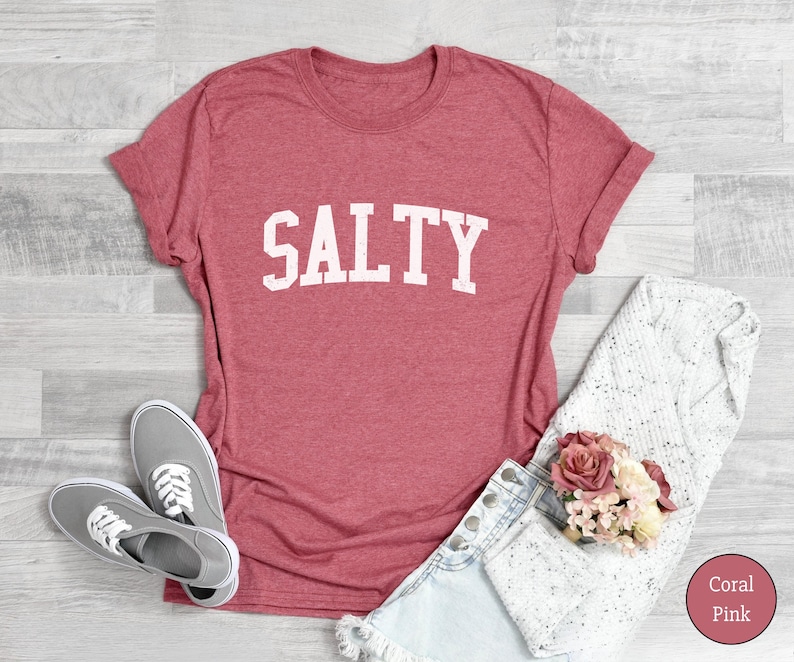 Puede incluir: Una camiseta de color coral con la palabra "SALTY" impresa en blanco en la parte delantera. La camiseta est&aacute; hecha de un material suave y c&oacute;modo y tiene un corte holgado.