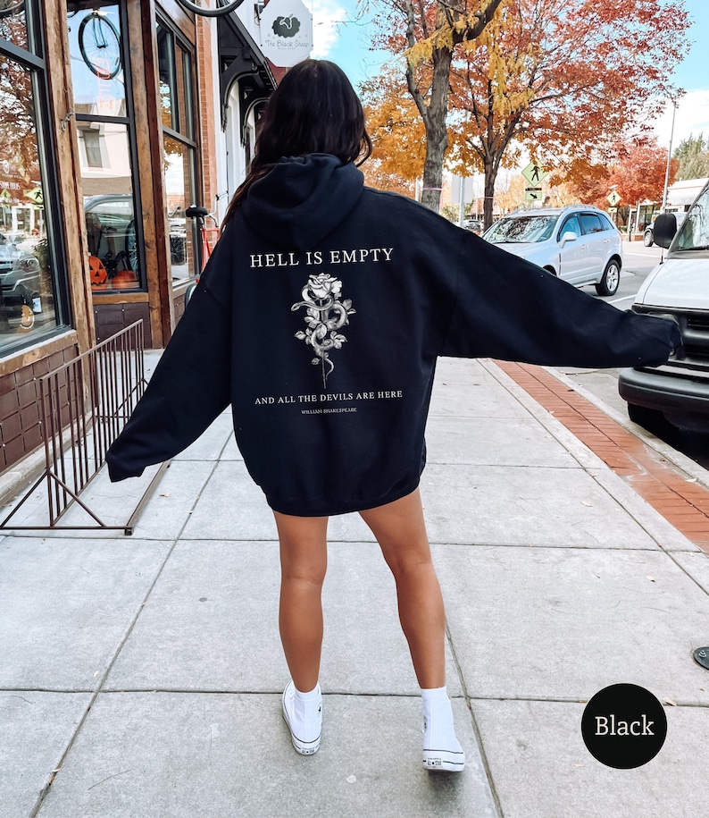 May include: Black hoodie with the text "HELL IS EMPTY" above a floral and snake design, and the quote "AND ALL THE DEVILS ARE HERE" below. The hoodie is worn by a person on a sidewalk.