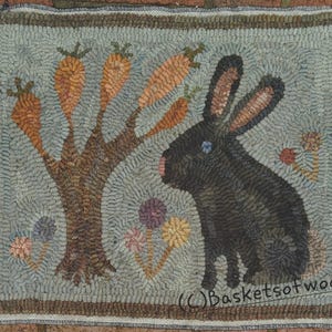May include: Hand-hooked rug featuring a black rabbit with a pink nose and blue eye, positioned next to a tree with orange carrots. The rug has a light blue background with colorful flowers and a brown border. The rug is rectangular.