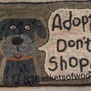 May include: Hand-hooked rug featuring a dog with a speech bubble. The dog is primarily dark gray with a brown collar. The speech bubble reads "Adopt, Don't Shop" in dark brown letters against a light pink and beige background.