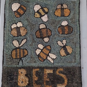 May include: Hand-hooked rug featuring a pattern of bees in shades of brown, tan, and white against a teal background. The word "BEES" is displayed in large, tan letters at the bottom. The rug has a dark border.