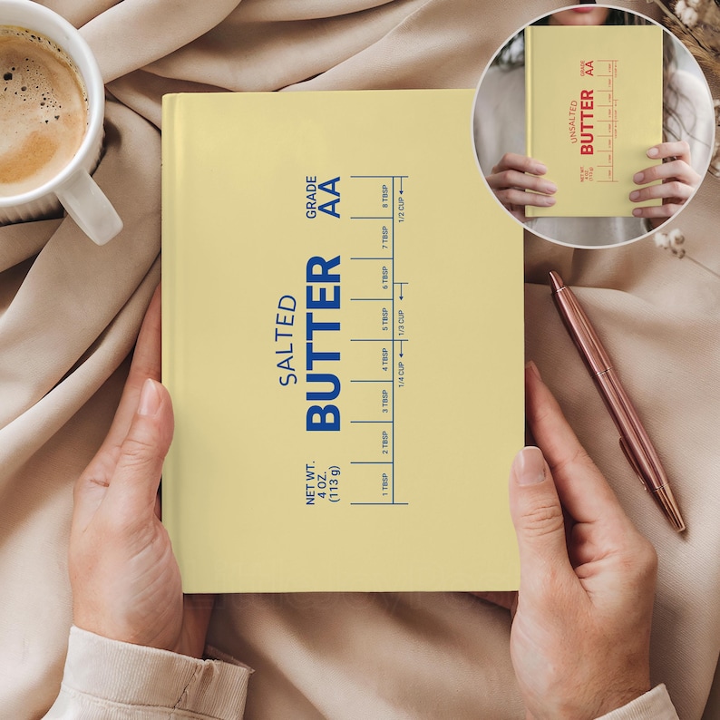 Puede incluir: Un cuaderno amarillo claro con las palabras "SALTED BUTTER" en azul. El cuaderno tiene una gu&iacute;a de medici&oacute;n para la mantequilla, con un peso neto de 113 g. Tambi&eacute;n se ven una taza de caf&eacute; y un bol&iacute;grafo.