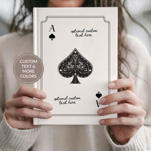 May include: A white hardcover book featuring a black ace of spades playing card design on the front cover. The cover includes the text 'optional custom text here' in two locations and a circular badge stating 'CUSTOM TEXT & MORE COLORS'.