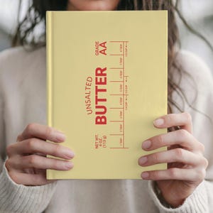 May include: A yellow notebook with the words "UNSALTED BUTTER" in red, along with measurement markings. The notebook also includes the text "NET WT. 4 OZ. (113 g)" and "GRADE AA".