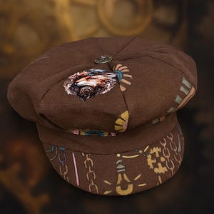 May include: Brown newsboy cap with a decorative button on top. The cap features a printed design with gears, chains, and other steampunk-inspired elements. The brim has a patterned design with chains and lightbulbs.