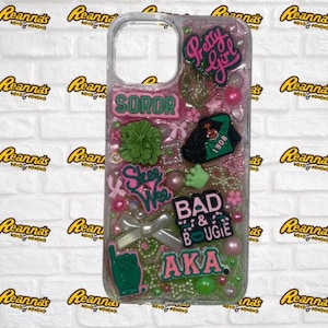 May include: Clear phone case decorated with pink, green, and white embellishments. The case features the words "Pretty Girl", "Soror", "Skee Wee", "Bad & Bougie", and "AKA". It also includes a green hand, a bow, and various charms.