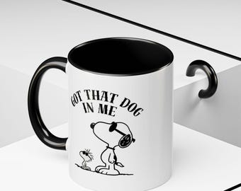 May include: White ceramic mug with a black interior and handle. The mug features a black and white illustration of Snoopy wearing sunglasses with the text "GOT THAT DOG IN ME".