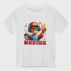 May include: White t-shirt featuring a colorful graphic of a cartoon character with headphones, sunglasses, and a game controller. The character is making a peace sign. The word "ROBLOX" is printed in red block letters below the character.