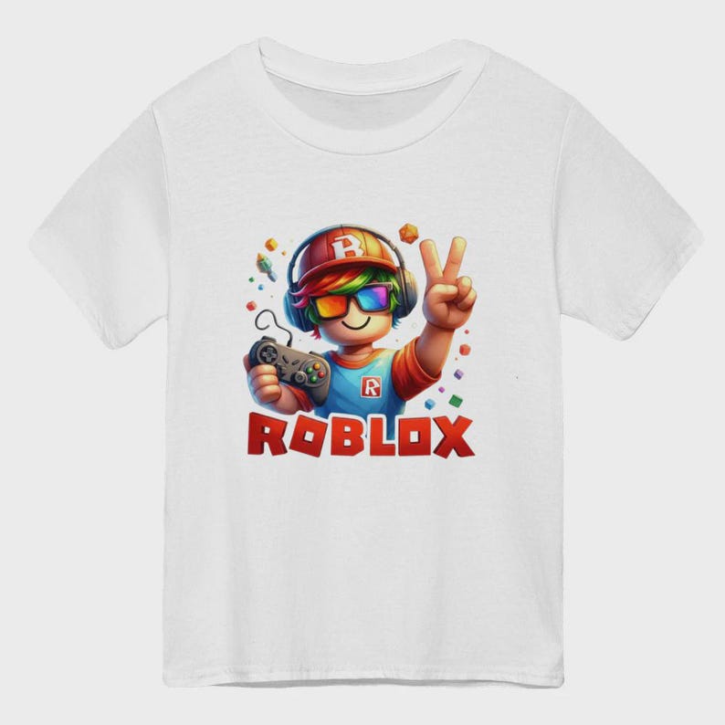 May include: White t-shirt featuring a colorful graphic of a cartoon character with headphones, sunglasses, and a game controller. The character is making a peace sign. The word "ROBLOX" is printed in red block letters below the character.