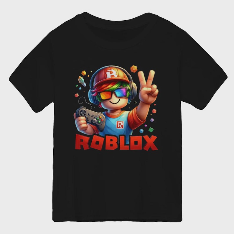 May include: Black t-shirt featuring a colorful illustration of a Roblox character holding a game controller and making a peace sign. The Roblox logo is displayed in red. The character wears a hat, headphones, and rainbow-colored glasses.