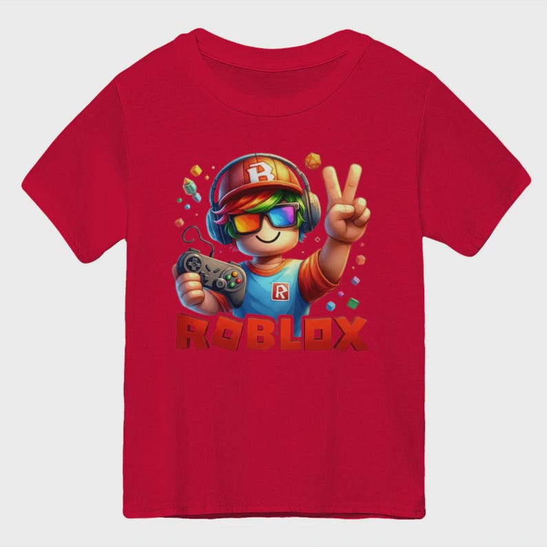 May include: Red t-shirt featuring a colorful graphic of a Roblox character wearing headphones and sunglasses, holding a game controller, and making a peace sign. The word "ROBLOX" is displayed in large, 3D letters below the character.