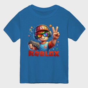 May include: Blue t-shirt featuring a cartoon character with a headset, rainbow glasses, and a controller. The character is giving a peace sign. The word "ROBLOX" is printed in red block letters.