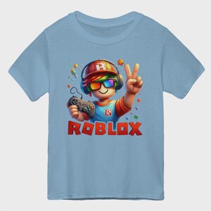 May include: Light blue t-shirt featuring a cartoon character with headphones, rainbow-colored glasses, and a controller. The character is giving a peace sign. The word "ROBLOX" is displayed in red block letters.