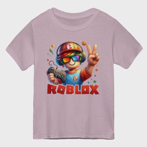 May include: A light pink t-shirt featuring a cartoon character with rainbow-colored hair, sunglasses, and headphones. The character is holding a game controller and flashing a peace sign. The word "ROBLOX" is printed in red.