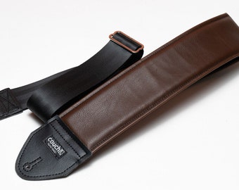 May include: A brown leather guitar strap with a black nylon strap and a black leather end piece with the word "Couch" printed on it.