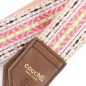 May include: A pink and white camera strap with a geometric pattern and a brown leather strap with the text "couch[n] hand made".
