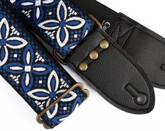 May include: A guitar strap with a black leather end and a blue and white patterned fabric strap. The strap has a brass buckle and a brass button.