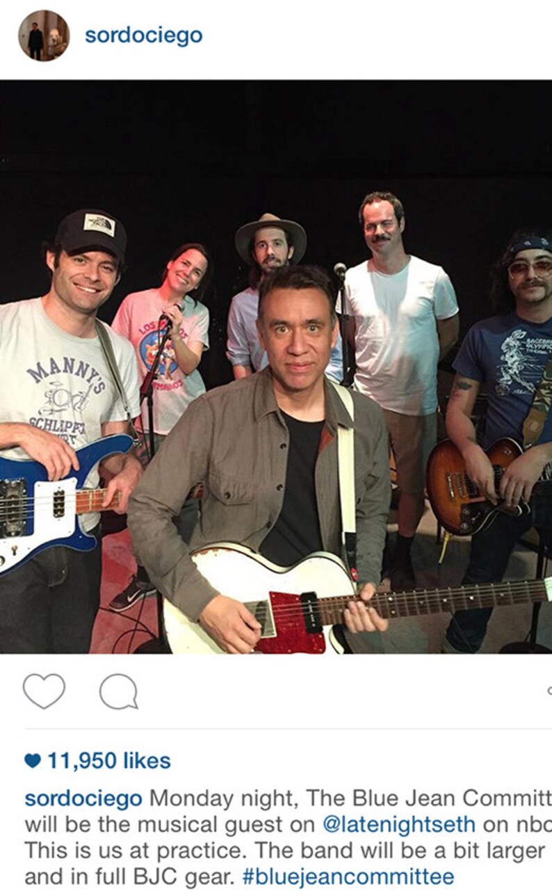May include: A group of musicians, The Blue Jean Committee, are shown in a rehearsal setting. The band members are holding guitars and microphones. The image includes the text "Manny's" on a t-shirt and the hashtag #bluejeancommittee.