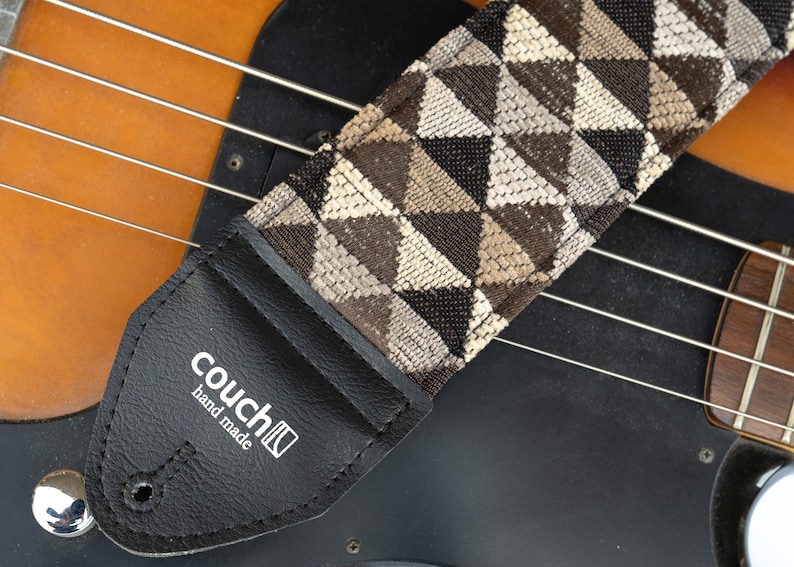 May include: A black and brown guitar strap with a geometric pattern. The strap is made of fabric and has a leather end with the text "couch" and "hand made".