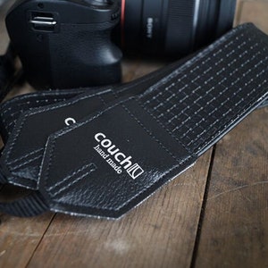 May include: Black leather camera strap with a white "couch" logo and the text "hand made".