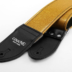 Pu&ograve; includere: Cinturino per chitarra con glitter dorati e estremit&agrave; in pelle nera. Il cinturino ha il testo "couch" e "hand made" stampato su un'estremit&agrave;.