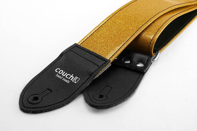 Pu&ograve; includere: Cinturino per chitarra con glitter dorati e estremit&agrave; in pelle nera. Il cinturino ha il testo "couch" e "hand made" stampato su un'estremit&agrave;.
