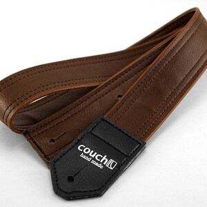 May include: Brown leather guitar strap with black stitching and a black leather patch with the text "couch hand made".