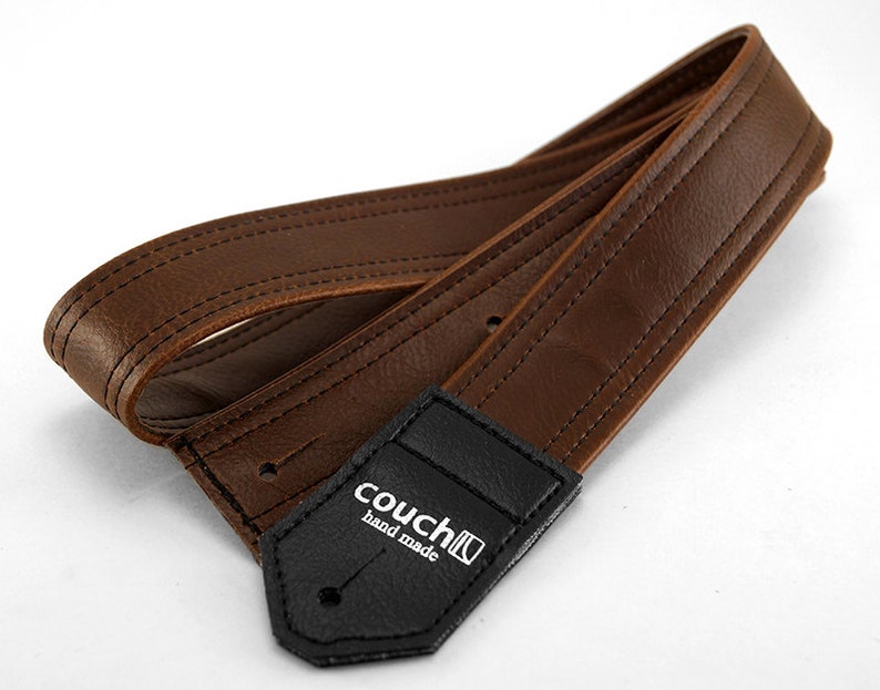 May include: Brown leather guitar strap with black stitching and a black leather patch with the text "couch hand made".