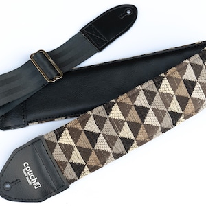 May include: A black and brown guitar strap with a geometric pattern and a black leather end with the text "couch" in white.