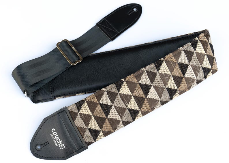 May include: A black and brown guitar strap with a geometric pattern and a black leather end with the text "couch" in white.