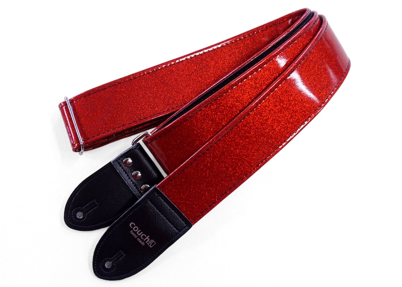 Pu&ograve; includere: Cinturino per chitarra rosso glitterato con estremit&agrave; in pelle nera e accessori argentati. Il cinturino &egrave; realizzato da Couch Guitars e riporta la scritta "Couch Guitars Handmade" sull'estremit&agrave;.