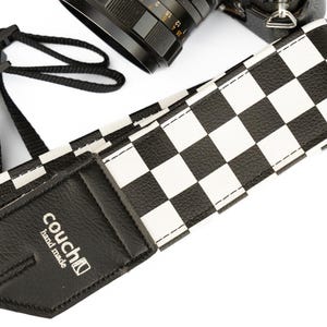 May include: Black and white checkered camera strap with a black leather patch that says "couch" and "hand made".