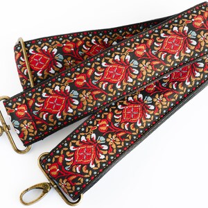 May include: A black and red patterned guitar strap with gold metal clasps. The strap has a floral design with red, gold, and white accents.