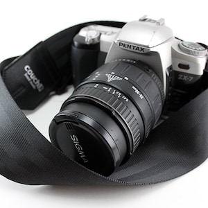 May include: A silver Pentax ZX-7 camera with a black Sigma 28-80mm lens attached. The camera is on a black camera strap.