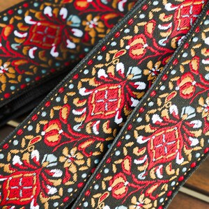 May include: Two black guitar straps with a colourful floral pattern in red, gold, white and blue. The straps have brass buckles.