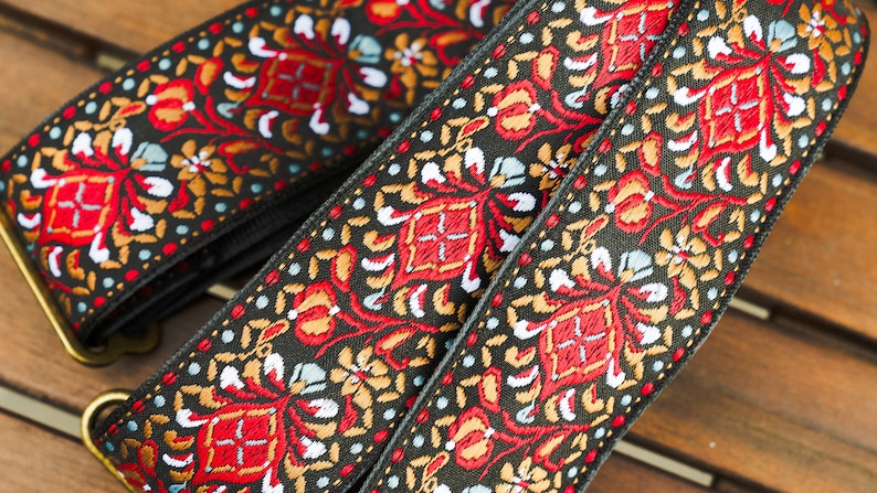 May include: Two black guitar straps with a colourful floral pattern in red, gold, white and blue. The straps have brass buckles.