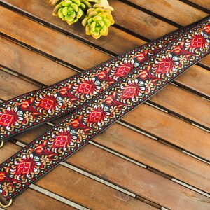 May include: A black and red woven strap with a floral pattern. The strap has gold metal hardware on each end.
