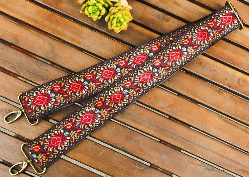 May include: A black and red woven strap with a floral pattern. The strap has gold metal hardware on each end.