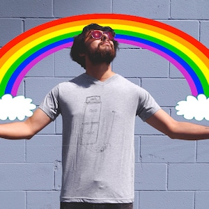 May include: A person wearing sunglasses stands in front of a brick wall with a rainbow and clouds drawn above them. The person is wearing a grey t-shirt with a drawing of a stereo system on it.