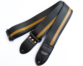 May include: Black guitar strap with two gold stripes and the text "couch" in white lettering. The strap is made of leather and has a buckle.