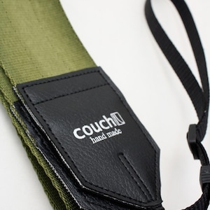 May include: Olive green guitar strap with a black leather end piece. The leather piece has the text "couch hand made" in white. A black strap with a loop is attached.