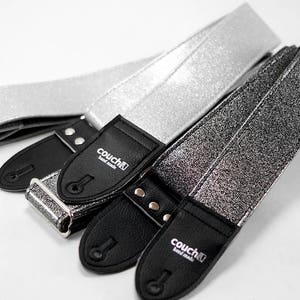 Pu&ograve; includere: Tre cinghie per chitarra con tessuto glitterato argento e estremit&agrave; in pelle nera. Le cinghie hanno il testo "couch" in lettere bianche sulle estremit&agrave; in pelle.