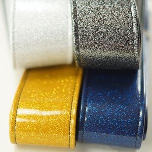 Pu&ograve; includere: Quattro rotoli di nastro glitterato in argento, oro, bianco e blu.