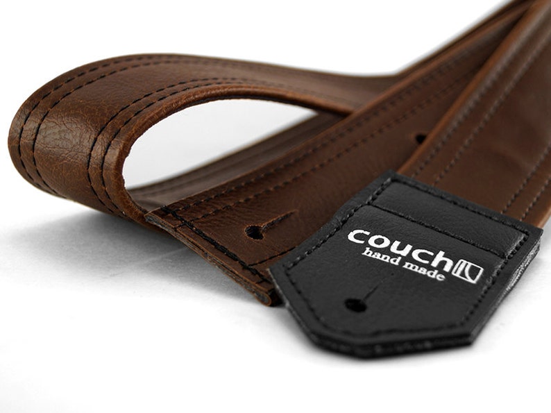 May include: Brown leather guitar strap with a black leather tag that says "couch hand made".