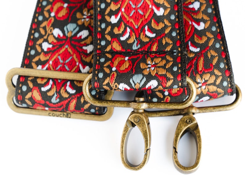 May include: A close-up of a black and red patterned fabric strap with gold metal hardware. The strap has the word "couch" printed on it.