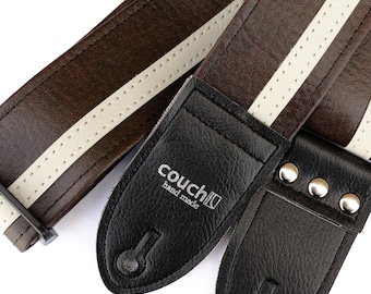 May include: Close-up of a brown and white guitar strap with a black leather end piece. The strap has a white stripe down the center and is made of leather. The black end piece has the text "couch hand made".
