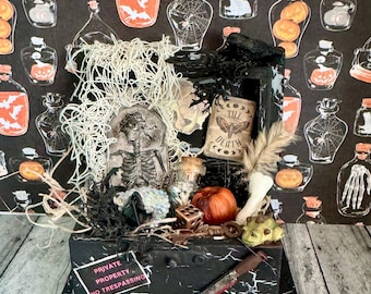 Może przedstawiać: Wystawa o tematyce Halloween z czarnym pudełkiem z różnymi upiornymi elementami. Zawiera szkielet, miniaturowe dynie, nóż i znak z napisem "PRIVATE PROPERTY NO TRESPASSING". Tło to czarna tapeta z butelkami z miksturami.