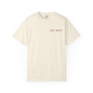 Puede incluir: Camiseta color crema con el texto "BUT WHY?" en fuente rojo oscuro. La camiseta de manga corta tiene cuello redondo y una etiqueta en la parte posterior del cuello. La camiseta está hecha de un material suave.